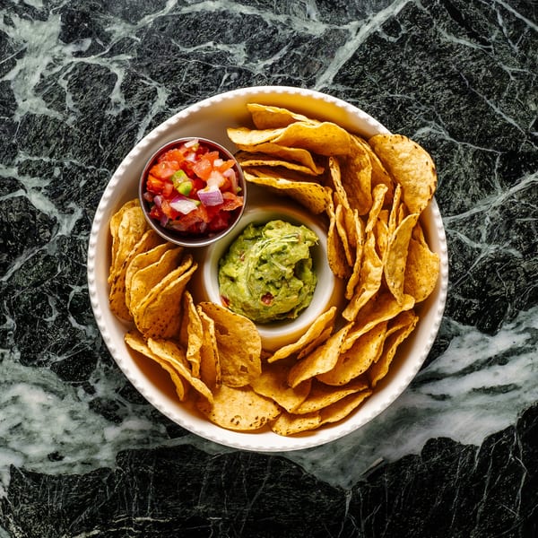 A white bowl filled with tortilla chips, guacamole, and pico de gallo on a marble surface.