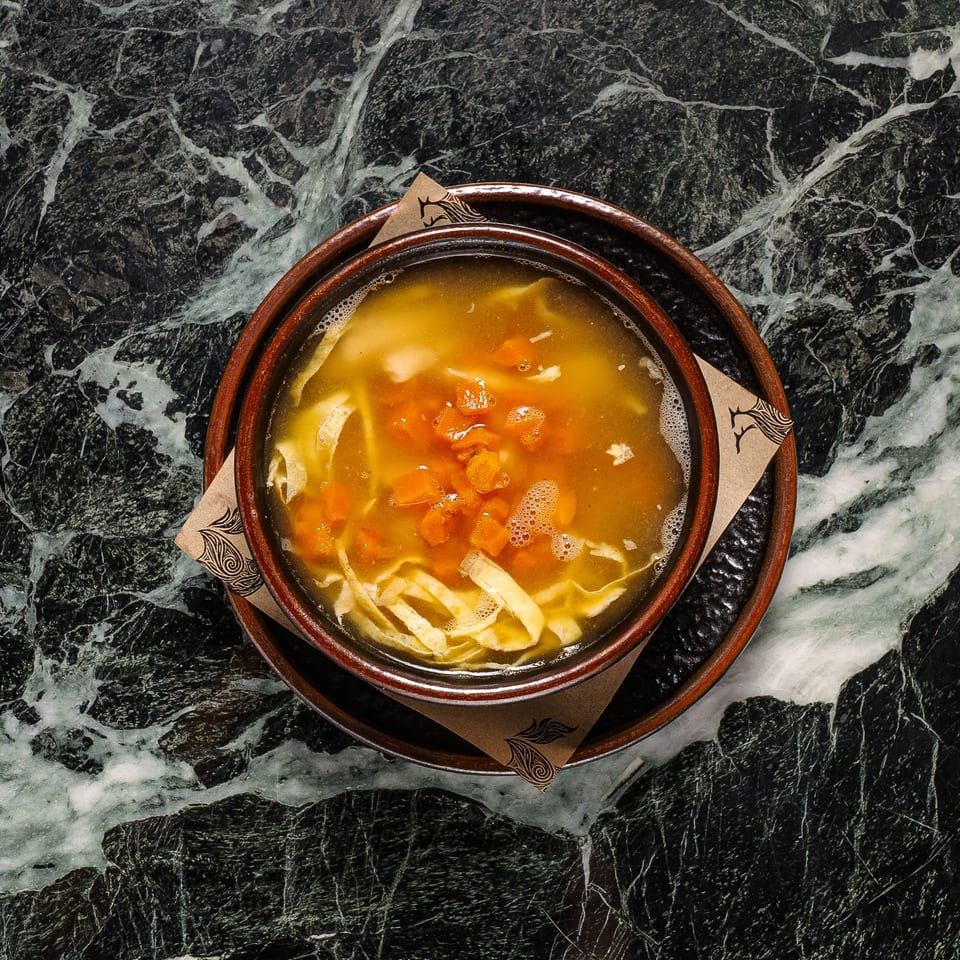 A bowl of chicken noodle soup with carrots and broth, served on a dark marble table.