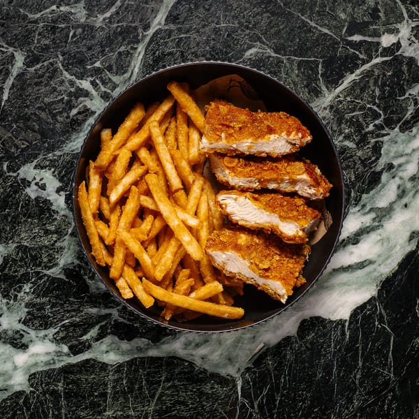 Crispy chicken tenders and golden french fries in a black bowl on a dark green marble surface.
