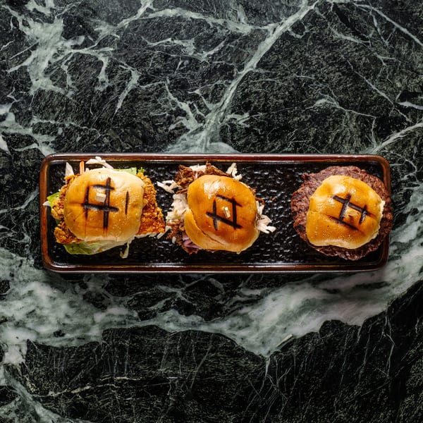 Three gourmet sliders, including fried chicken, pulled pork, and beef, on a dark marble surface.