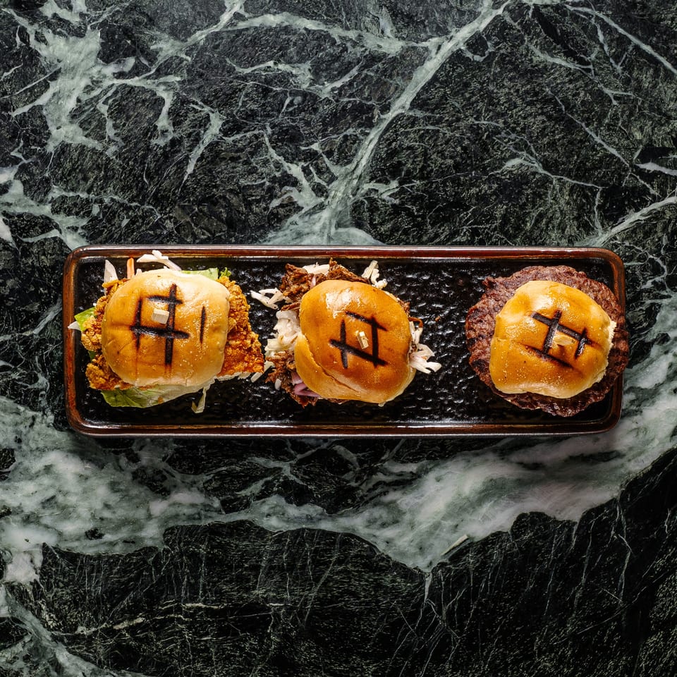 Three gourmet sliders, including fried chicken, pulled pork, and beef, on a dark marble surface.