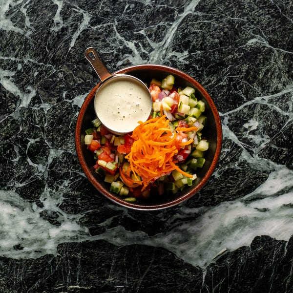 Overhead view of a chopped salad with shredded carrots and a side of dressing on a marble surface.